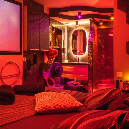 Chambre de la love room La Boudoir à Ferney-Voltaire proche d'Annemasse avec vidéoprojecteur, fauteuil Tantra et ambiance romantique.